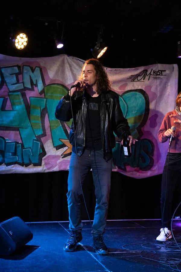 Performerin steht mit Mikrofon vor einem Graffiti-Banner